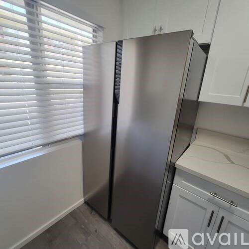 A stainless steel refrigerator stands in a kitchen with white cabinets.
