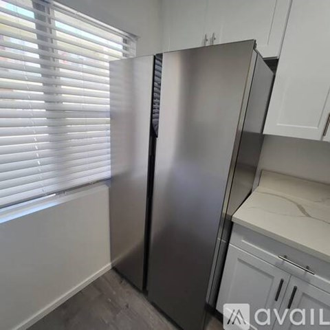 A stainless steel refrigerator stands in a kitchen with white cabinets.
