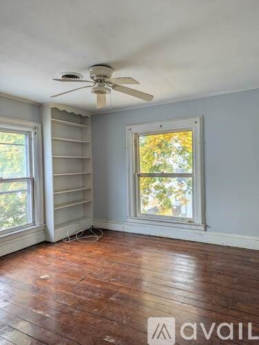 A room with a ceiling fan and two windows.