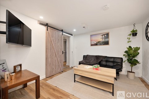 A living room with a black couch, a wooden table, a flat screen TV, and a plant.