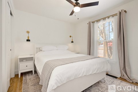 A bedroom with a large bed, a ceiling fan, and a window with curtains.