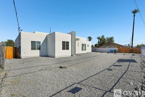 A gravel lot with a white building and a palm tree in the background.