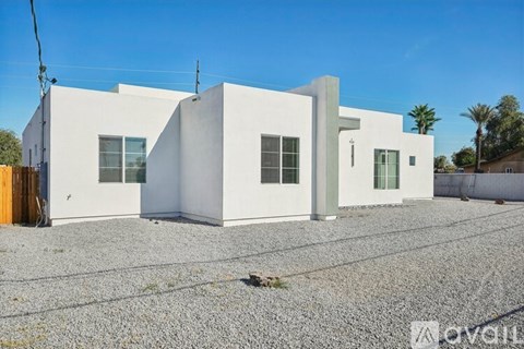 A white modern house with a gravel driveway in front.