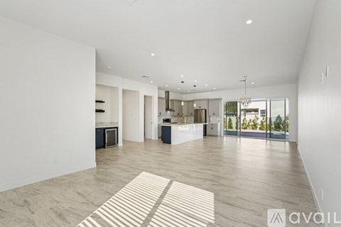 A spacious living room with a large rug on the floor and a kitchen area in the background.