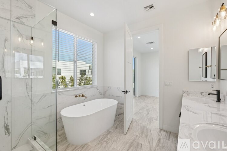 A bathroom with a white tub and sink, a glass shower door, and a large window.