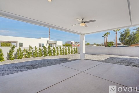 A patio with a ceiling fan and a view of a street with palm trees.