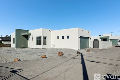 A white building with a green door and windows is surrounded by gravel and rocks.