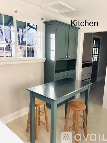 A kitchen with a dark green cabinet and a table with two stools.