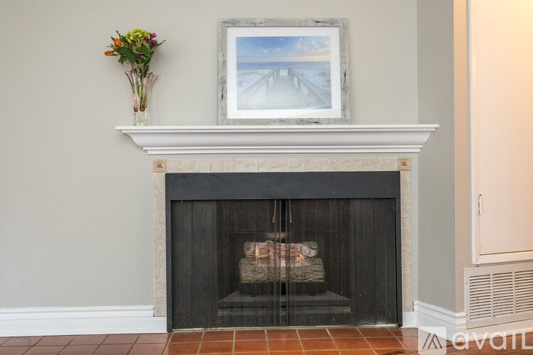 A fireplace with a painting above it and flowers in a vase on the mantle.