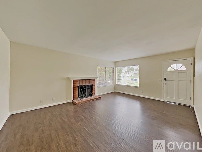 A spacious room with a fireplace and wood flooring.