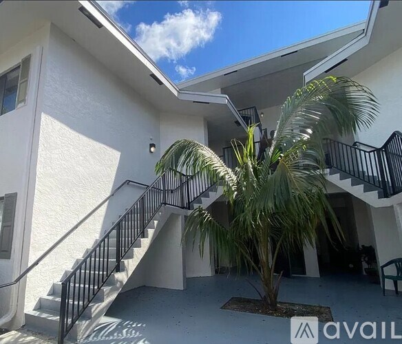 A palm tree is in front of a white building with a black railing staircase.