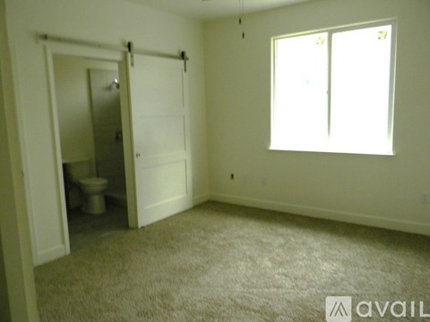 A carpeted room with a toilet in the doorway and a window on the wall.
