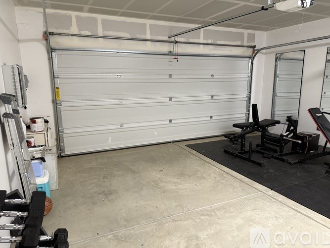 A garage with a white roller shutter door and a black weight bench.