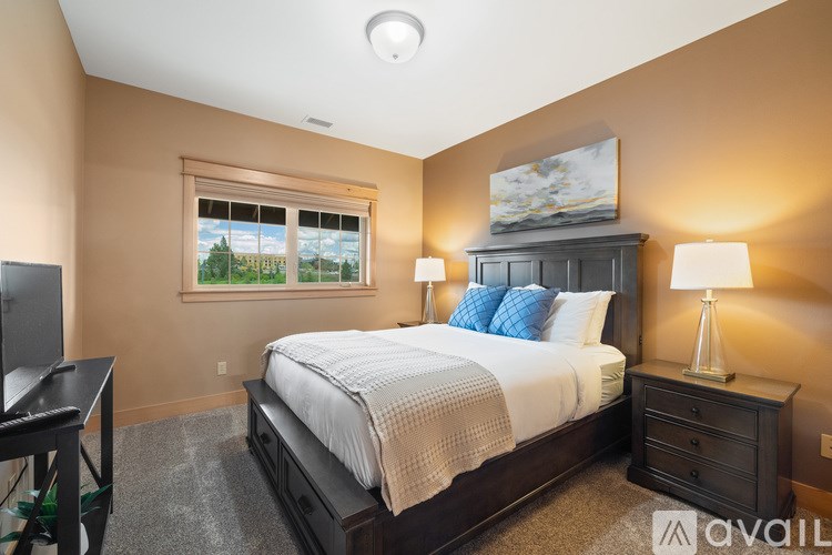 A bedroom with a large bed, a nightstand with a lamp, and a window with a view of trees.