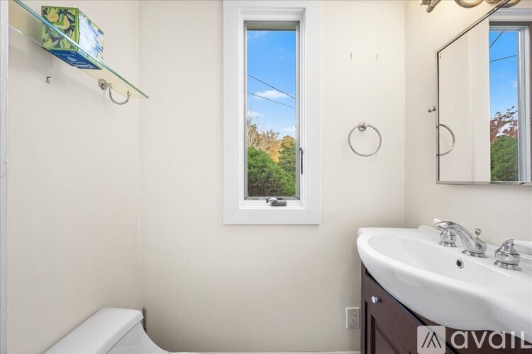 A bathroom with a toilet, sink, mirror, and a window.
