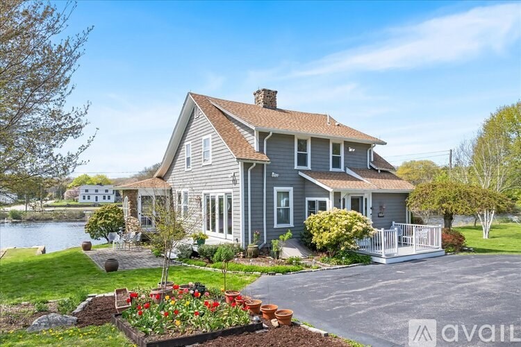 A house with a grey exterior and a red roof is surrounded by a well-kept lawn and a flower bed.