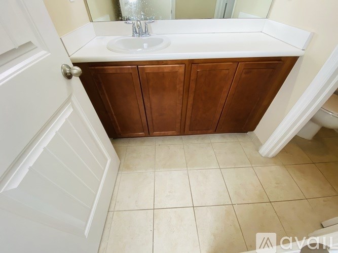 A white door is open to a bathroom with a sink and wooden cabinets.