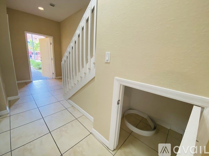 A hallway with a toilet in a cabinet under the stairs.