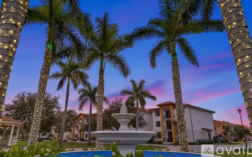 A fountain is in the middle of a grassy area with palm trees on either side.