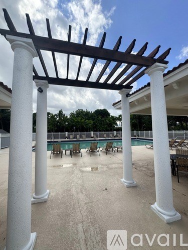 A pool area with a pergola and chairs.