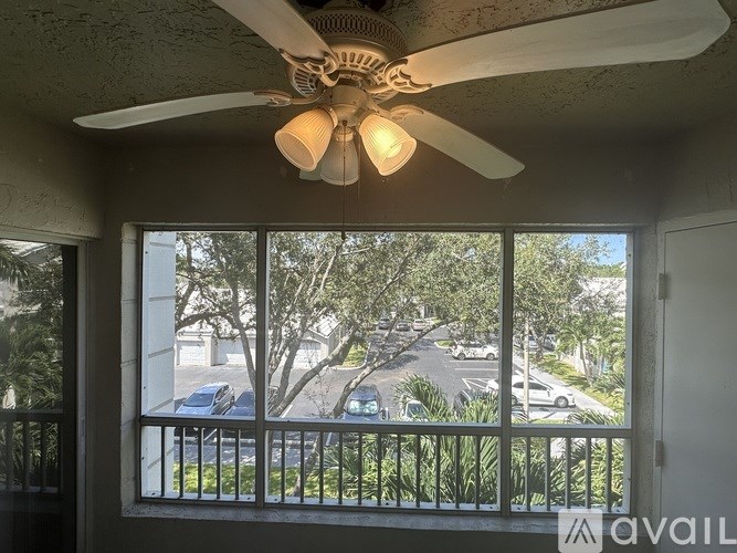 A room with a ceiling fan and a window overlooking a parking lot.