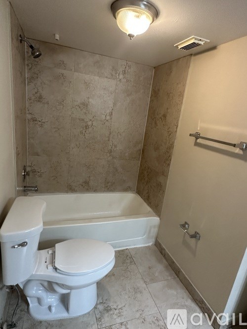 A white toilet sits in a bathroom with a marble wall and a white bathtub.