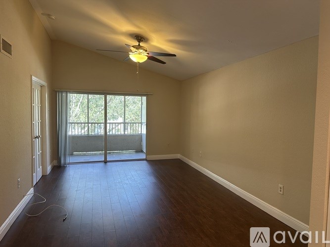 A spacious room with a ceiling fan and sliding glass doors leading to a balcony.