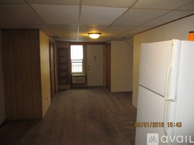 A room with a white fridge and a window with blinds.