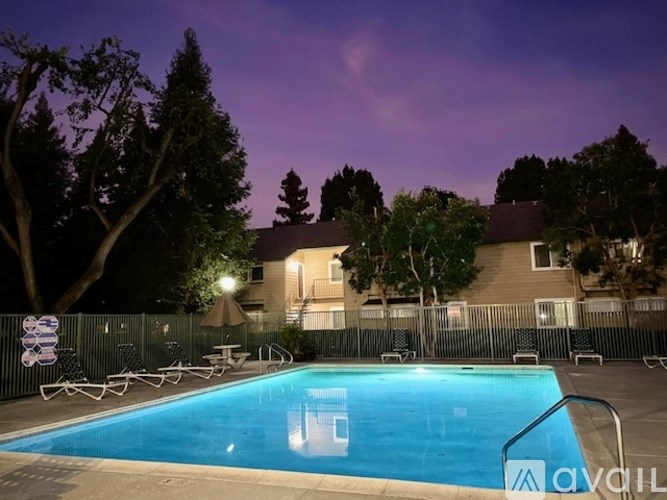 A swimming pool surrounded by a fence and trees at dusk.