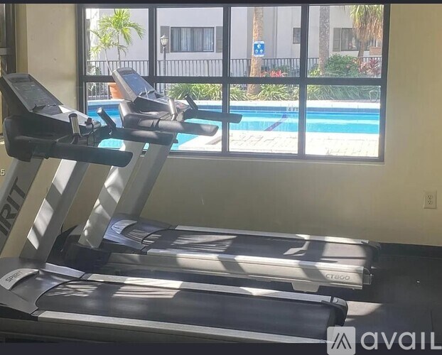 A treadmill in a room with a view of a pool and palm trees outside the window.