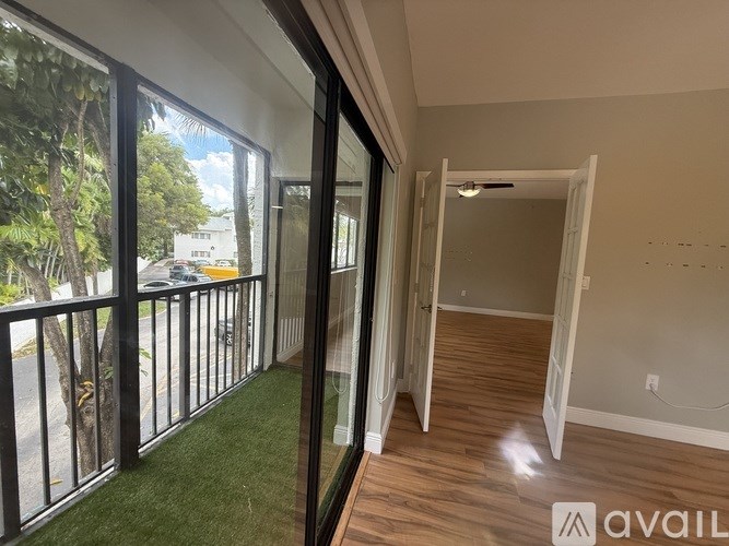 A balcony with glass doors leading to an empty room with wooden flooring.