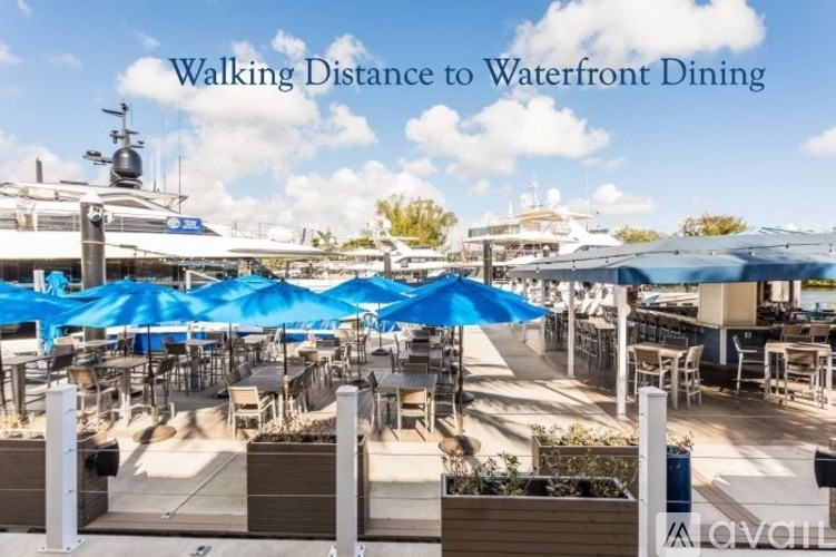 A waterfront dining area with tables and chairs under blue umbrellas.