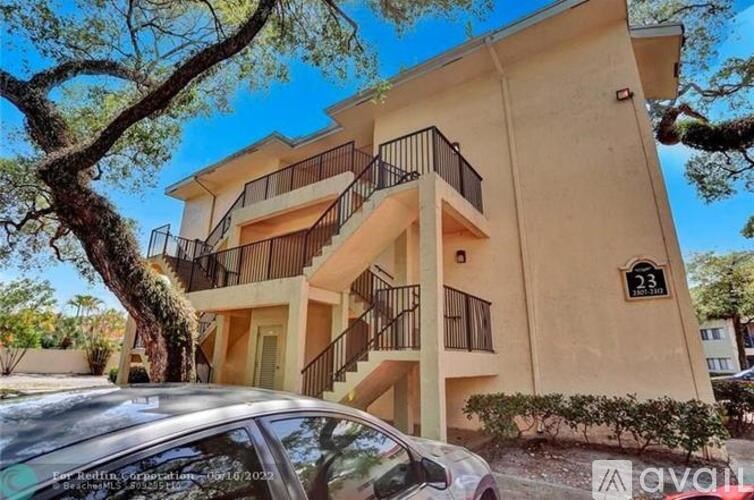 A beige apartment building with a balcony and a tree in front.