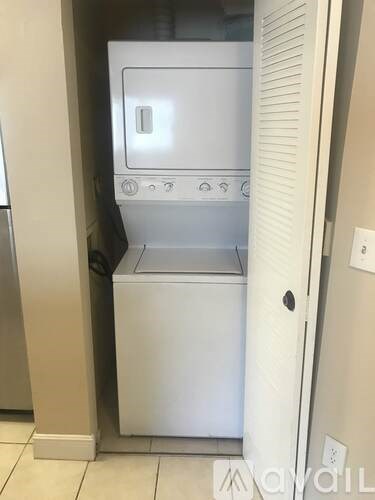 A white dishwasher is in a narrow space between a refrigerator and a wall.