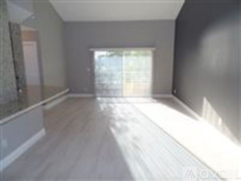 A spacious room with wooden flooring and a large window letting in natural light.