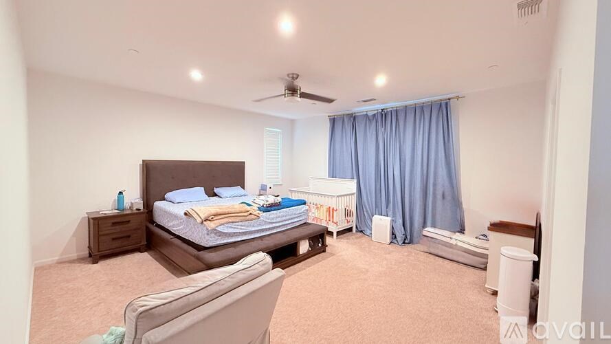 A bedroom with a bed, nightstand, chair, and window with blue curtains.
