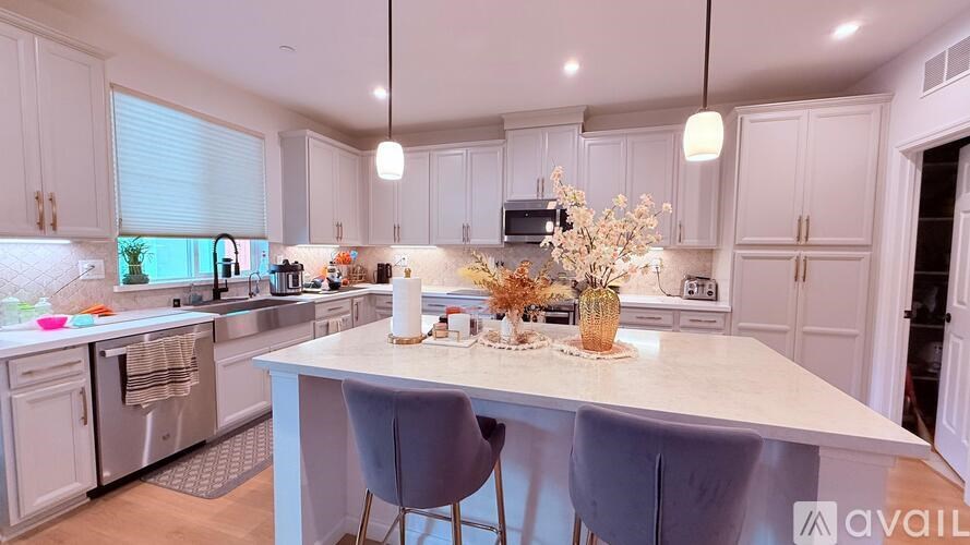 A kitchen with a white island and grey chairs.
