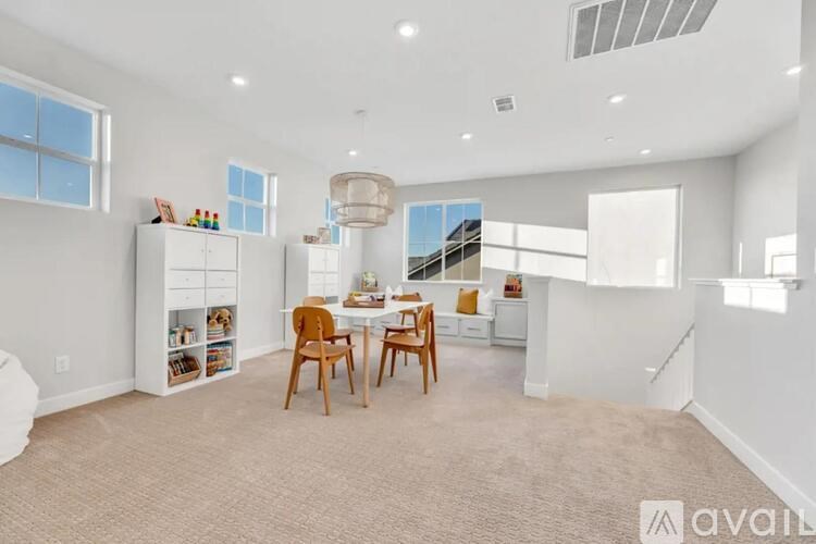 A well-lit, spacious room with a dining table set up with chairs and a bookshelf.