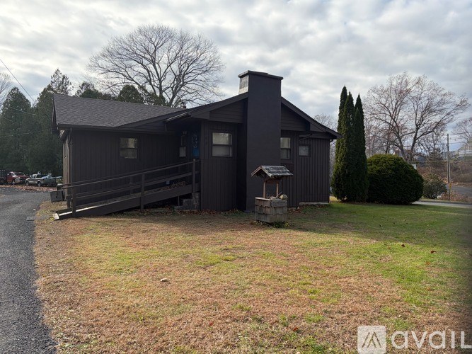 A house with a dark grey exterior and a chimney is surrounded by a grassy area and trees.