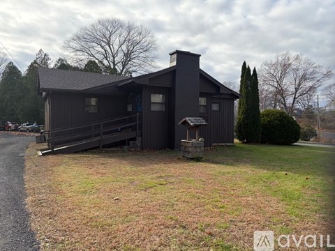 A house with a dark grey exterior and a chimney is surrounded by a grassy area and trees.