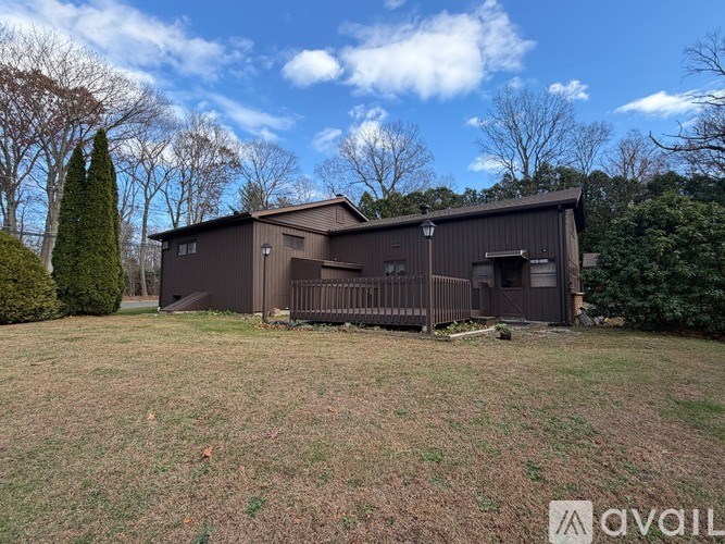 A large brown building with a porch is surrounded by a grassy field and trees.