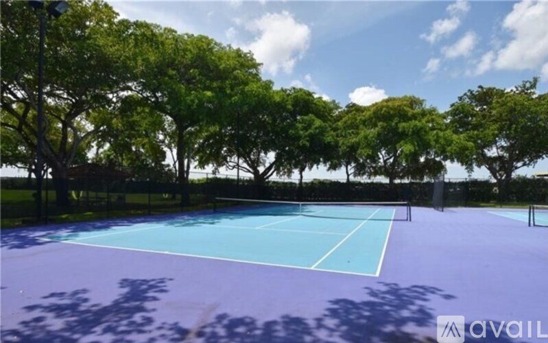 A tennis court surrounded by trees under a blue sky.