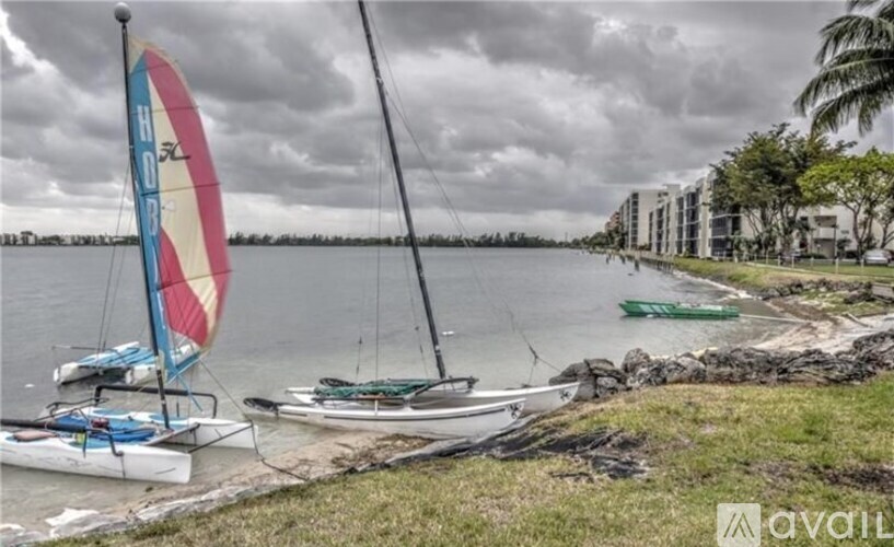 A sailboat with a red, white and blue sail is docked at a beach.
