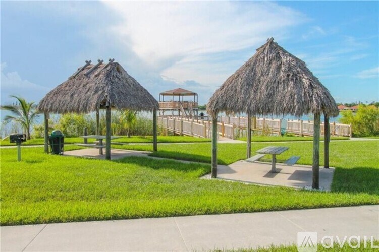 Two thatched-roof structures are situated in a grassy area with a bench and a picnic table nearby.