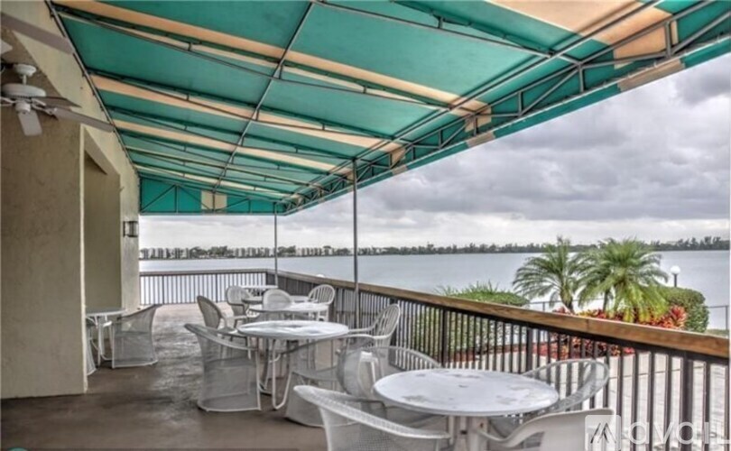 A patio with white furniture and a green awning overlooking a body of water.