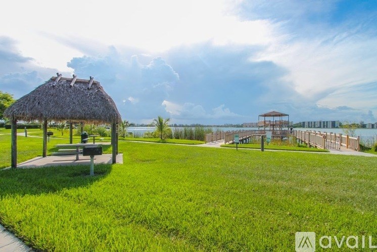 A grassy area with a thatched roof pavilion and a wooden deck overlooking a body of water.