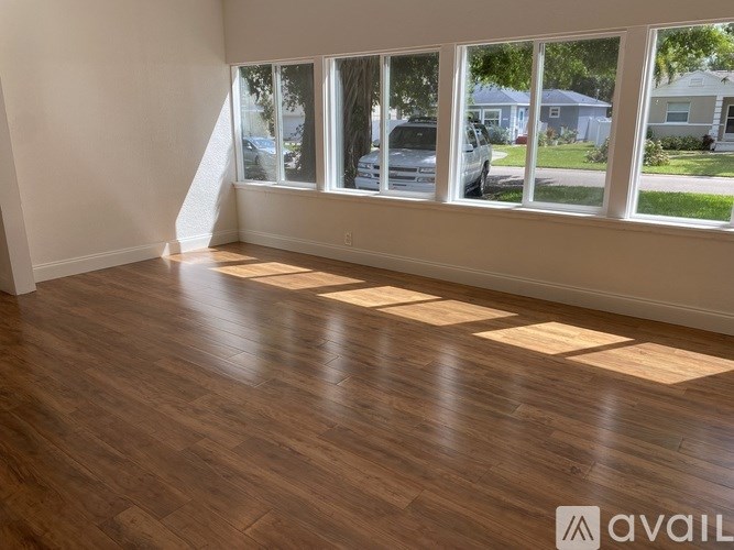 A room with wooden flooring and large windows overlooking a street.