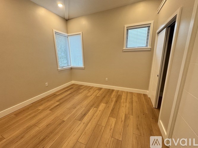 A room with wooden flooring and two windows.