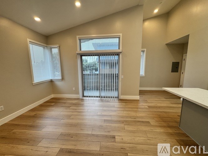 A spacious room with wooden flooring and a sliding glass door leading to a balcony.