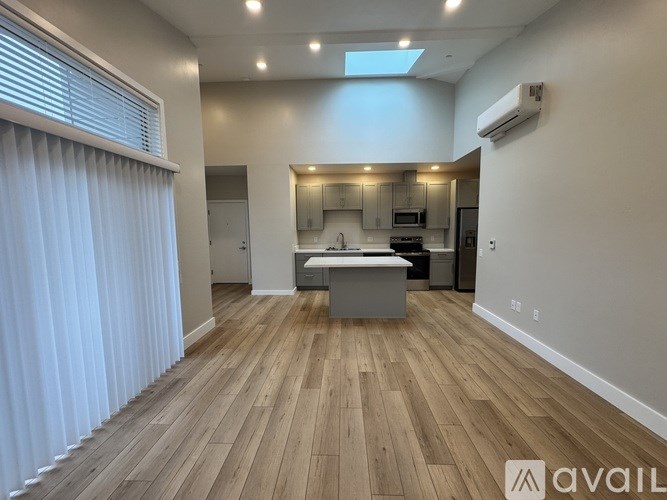 A spacious room with wooden flooring and a kitchen area in the background.